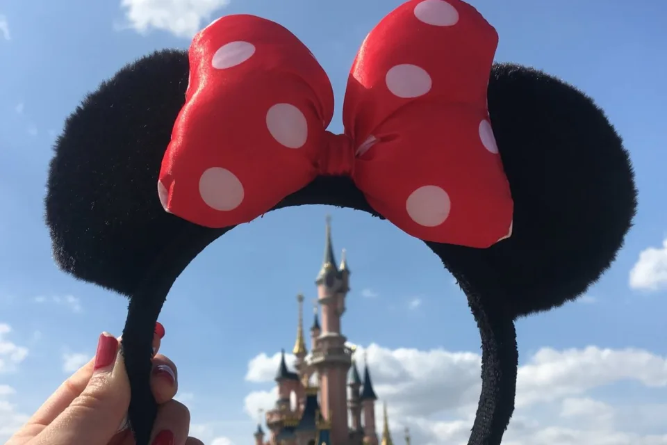 Cât costă un bilet la Disneyland O fată ține o bentiță cu mini urechi de șoarece.
